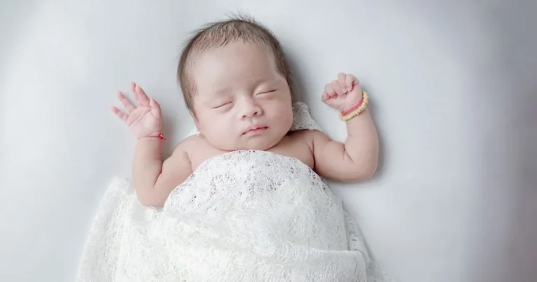 Swaddled baby with arms raised during sleep, illustrating Moro reflex often seen when baby wakes up when put down