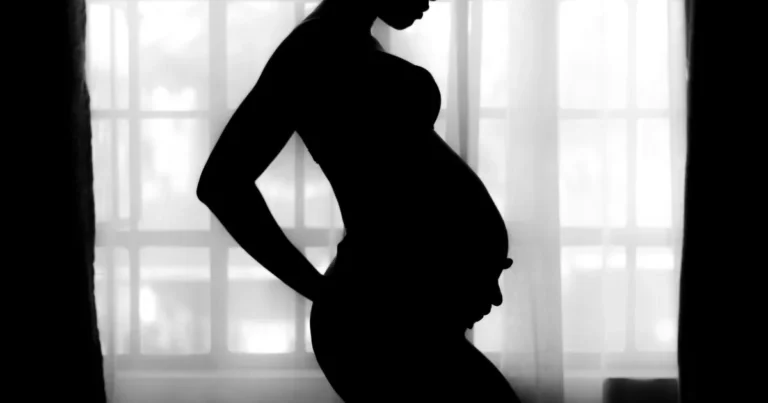 Silhouette of a pregnant woman standing in profile against a softly lit window, hands resting on her lower back ,why does my tailbone hurt