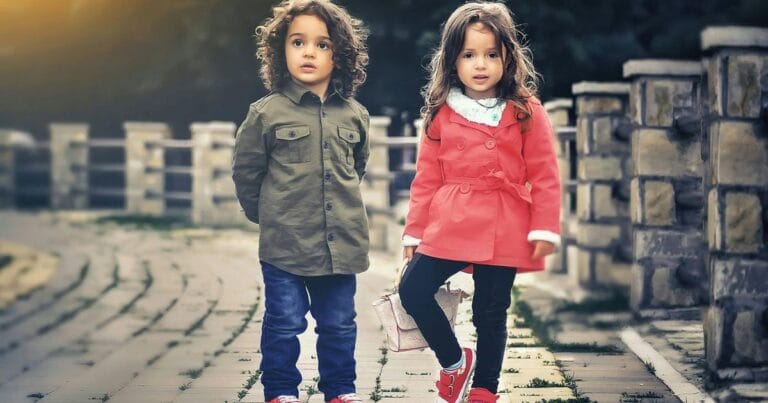 Two stylish toddlers with curly hair walking outdoors on a paved path in autumn, wearing trendy jackets and red shoes, Mixed Baby Names for Boys and Girls