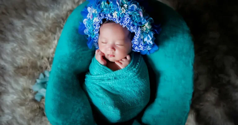 Newborn baby wrapped in teal fabric with a vibrant blue flower crown, peacefully sleeping , flower names for girls.