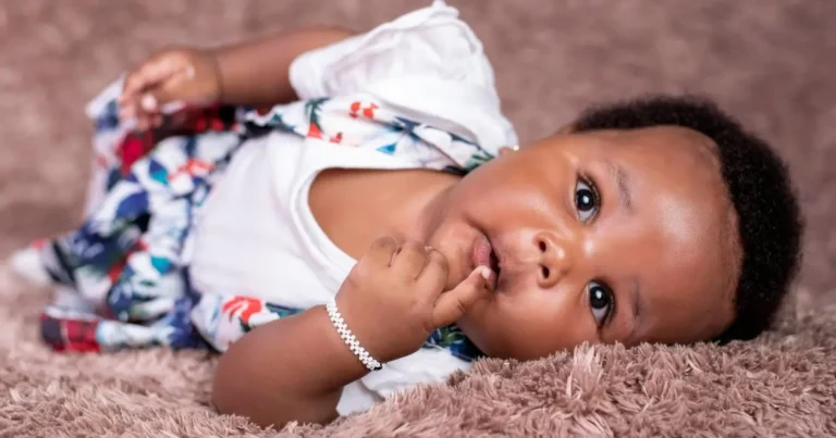 Adorable baby girl in patterned dress and bracelet lying on soft rug, expressing vibrant spirit of African names for girls