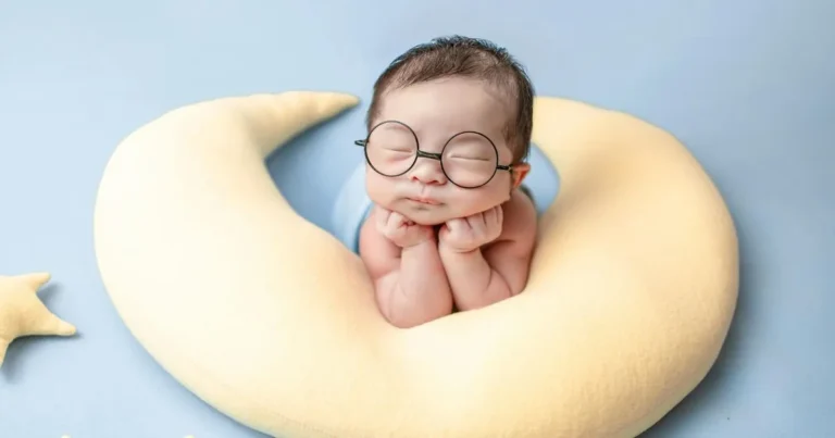 Newborn baby wearing round glasses peacefully resting inside a soft crescent moon pillow, evoking a dreamy and whimsical theme ,newborn sleeping in boppy pillow