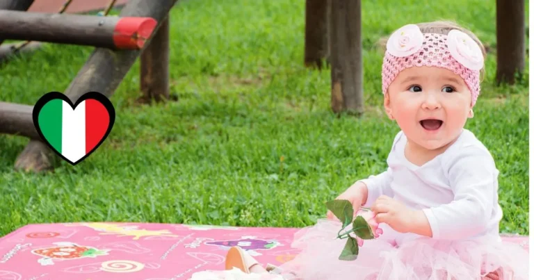 Smiling baby girl wearing pink headband sitting outdoors beside Italian flag heart, representing heritage and inspiration for an Italian name woman