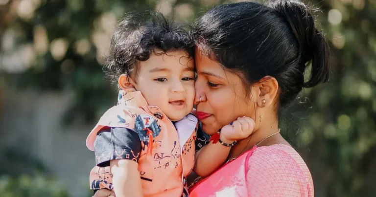A young mother lovingly holds her smiling baby boy, gently nuzzling her nose against his cheek while standing outdoors in soft sunlight ,cherokee boy indian names