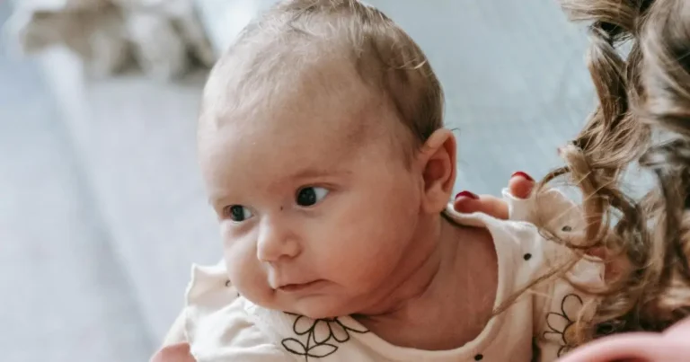 Baby with light hair looking sideways while being gently held names that start with m