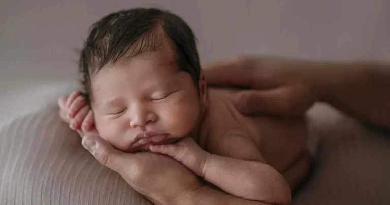 Newborn infant sleeping on side with head cradled in parent's hand, symbolizing safety and warmth for content on infant sleeping on side