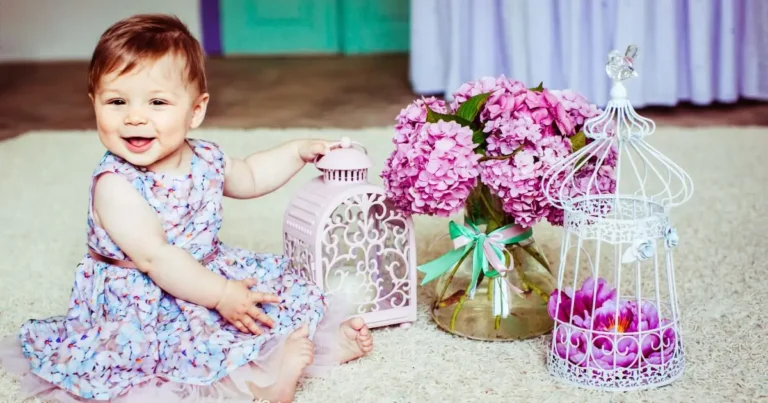 Smiling baby girl in floral dress beside pink hydrangeas, symbolizing elegance and sweetness of flower names for girls
