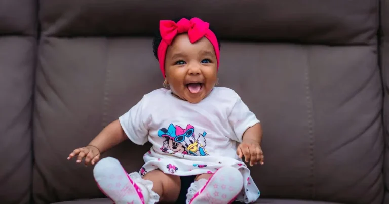 Baby girl with red bow and cartoon outfit laughing brightly, perfect visual for r girl names with bold personality