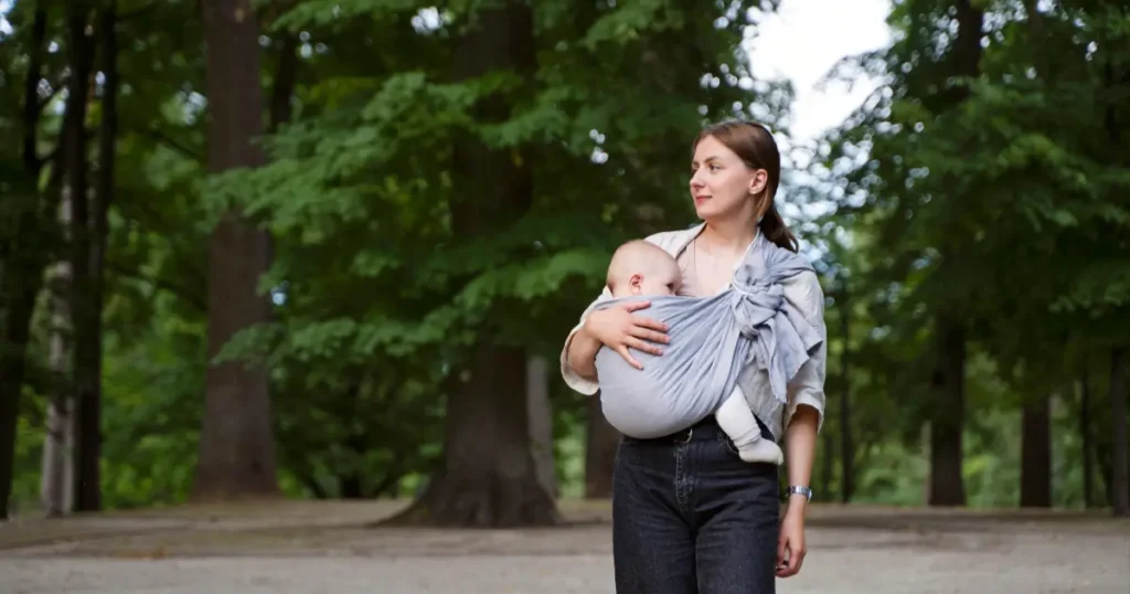 A woman holds her baby outdoors, comfortably wrapped in a linen baby wrap, enjoying the fresh air and sunshine.