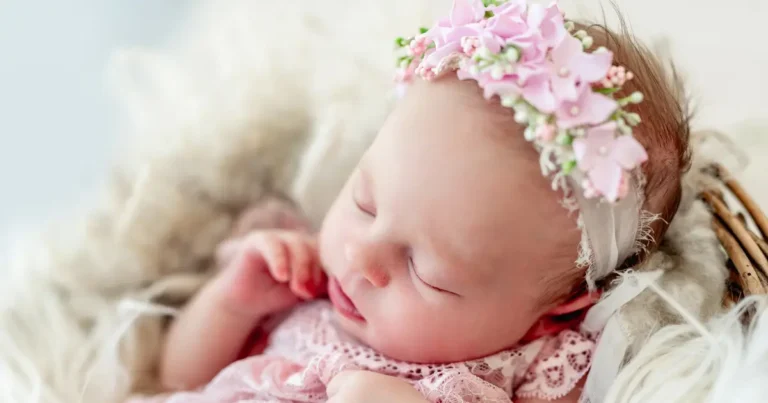 Newborn baby girl sleeping peacefully, dressed in pink lace and floral headband perfect inspiration for E names for girls