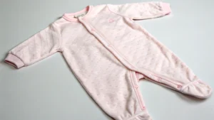 Light pink baby sleeping suit with long sleeves and snap buttons, laid flat on a surface.