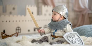 A baby dressed as a medieval knight with a tiny silver helmet and soft armor, holding a toy sword, sitting on a blanket with a castle-themed background, Knight Names