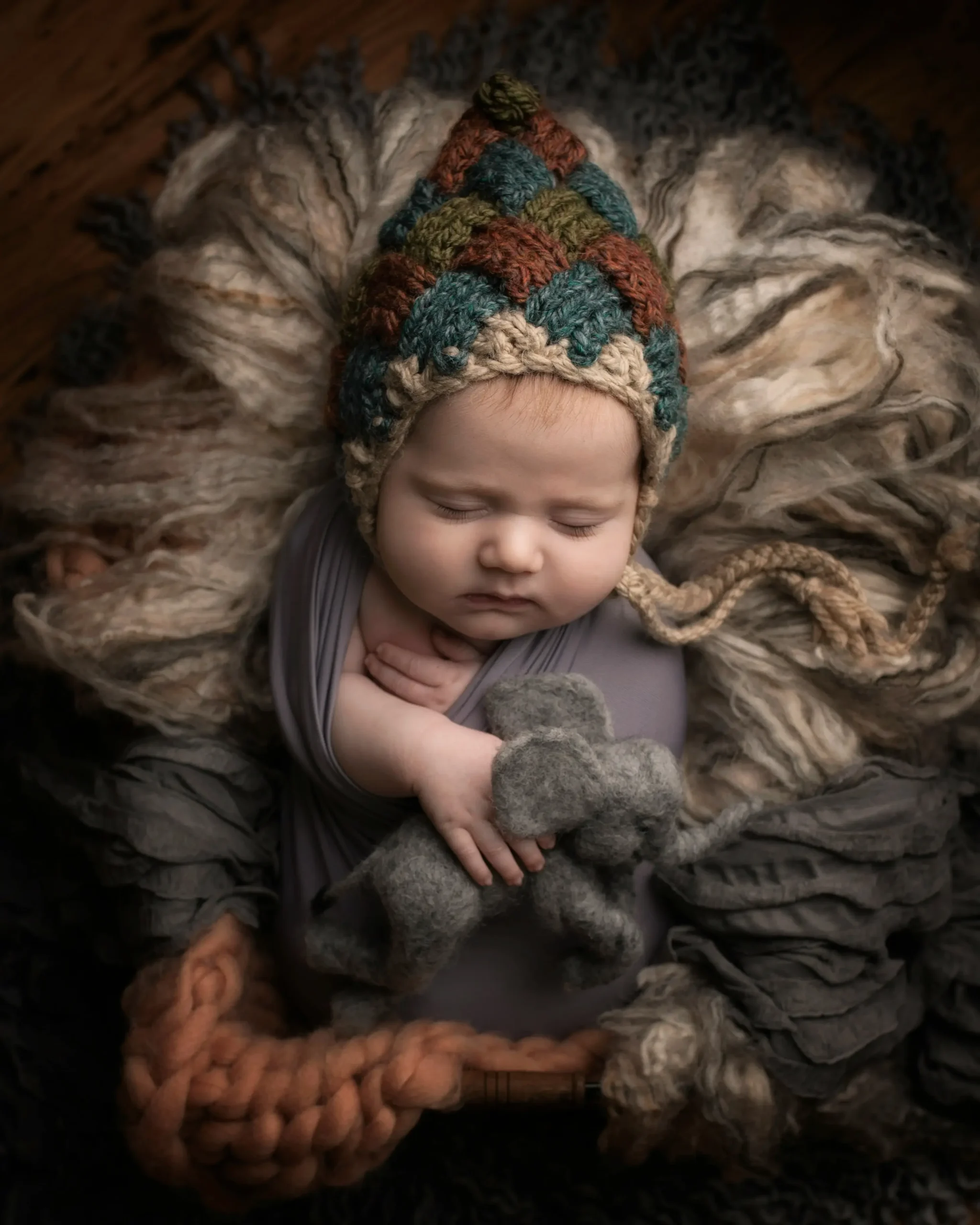 A baby boy sleeping with a knitted hat and a plush elephant toy.